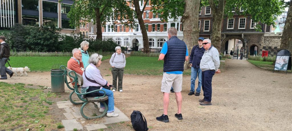 Tour guide Clive Lotherington explains the secrets of London to a tour group in a park.